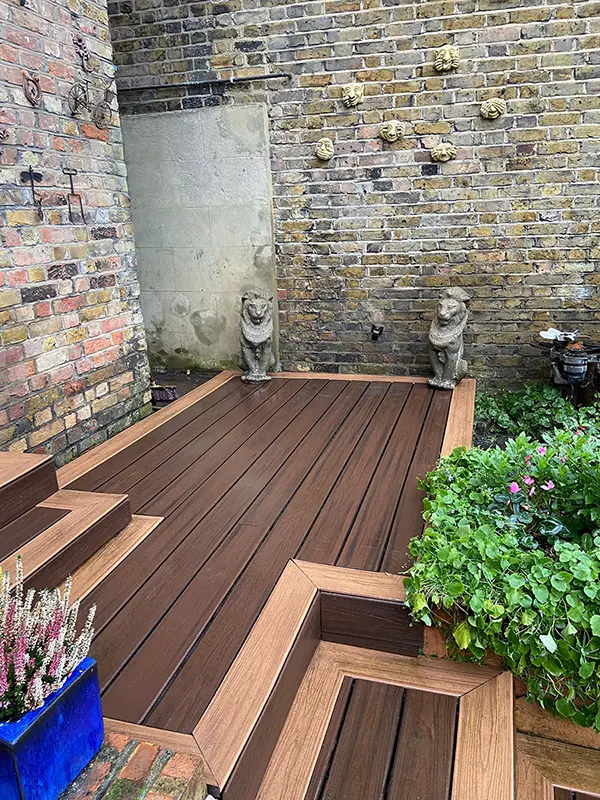 Composite decking Kingston - brown boards with framed edges and steps in a brick-walled garden Composite decking Kingston - brown boards with framed edges and steps in a brick-walled garden